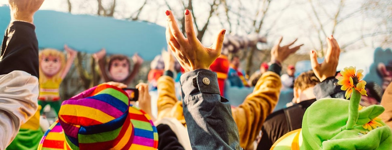 Viele Menschen strecken bei einer Veranstaltung im Freien ihre Hände in die Luft. Sie tragen bunte Hüte und Kostüme.