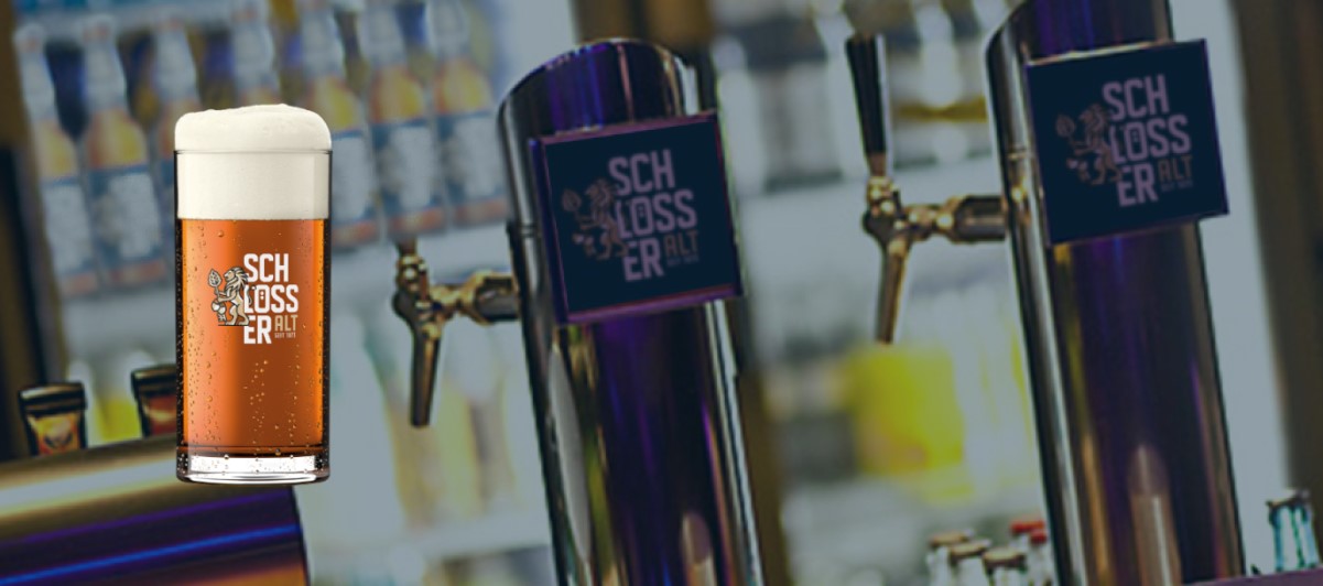 Ein Bierglas mit bernsteinfarbenem Bier steht im Vordergrund, dahinter Zapfhähne an einer Bar.